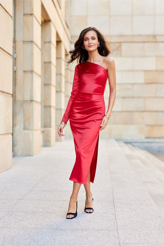 Female model walking forward in a red satin one-shoulder midi dress with a side slit against a pale stone columned facade background
