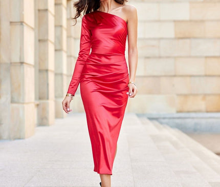 Model in a red satin one-shoulder long-sleeve bodycon midi dress walking down a light stone walkway in front of a beige columned wall