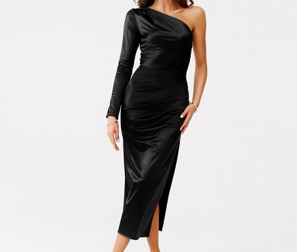 A model standing against a white backdrop wearing a black satin one-shoulder long-sleeve midi dress with a side slit