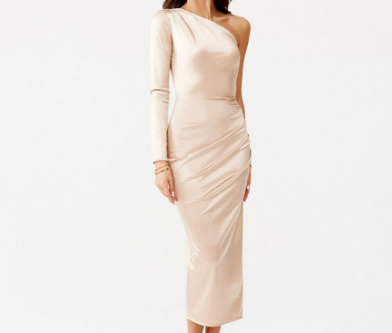 A female model stands in a white studio wearing a one-shoulder long-sleeve satin bodycon midi dress in soft nude beige with weight shifted to one leg and hands relaxed by her sides