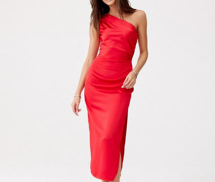 She stands in a slight walking pose against a plain white backdrop wearing a red satin one-shoulder midi dress with a side slit