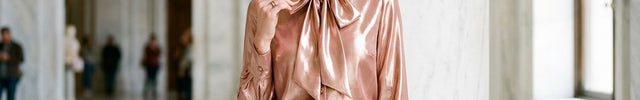 Woman in a rose gold blouse and black pants standing in a marble hallway